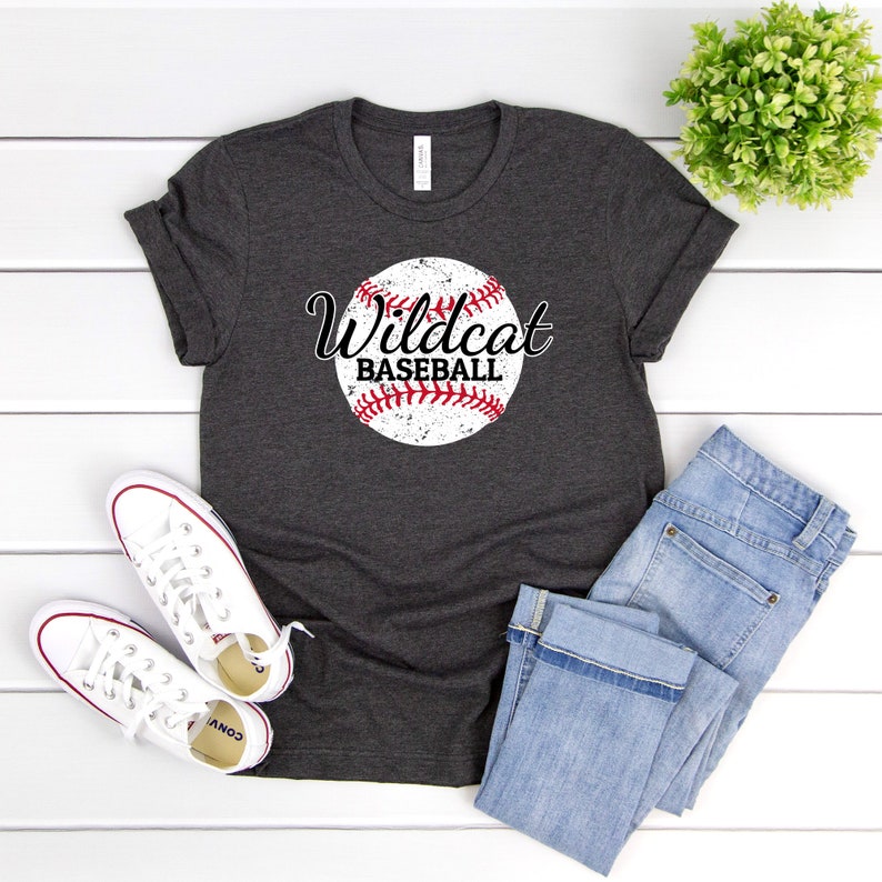 May include: A dark gray t-shirt with a white baseball graphic and the text "Wildcat Baseball" in black lettering.