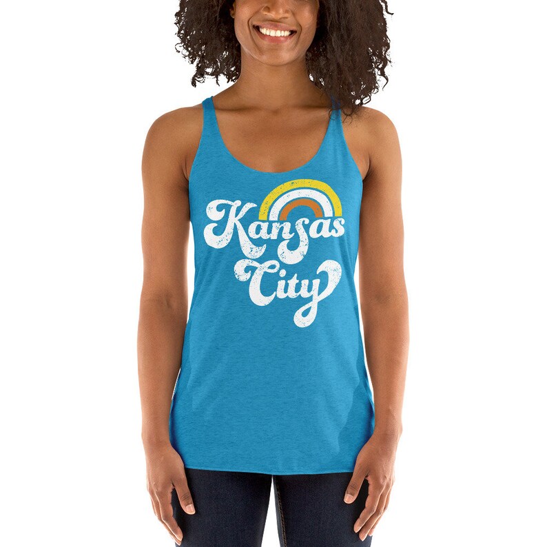 Puede incluir: Un top de tirantes azul turquesa con un gr&aacute;fico blanco desgastado que dice "Kansas City" con un arco&iacute;ris sobre el texto.