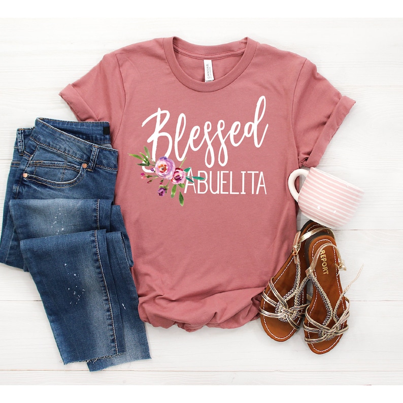 May include: A dusty rose t-shirt with the text "Blessed Abuelita" in white with a floral design.