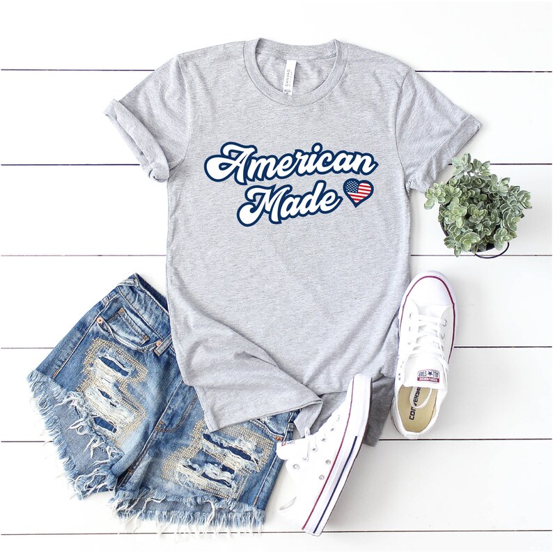 May include: A gray t-shirt with the text "American Made" in a retro font. A red, white, and blue heart with a small American flag design is next to the text.