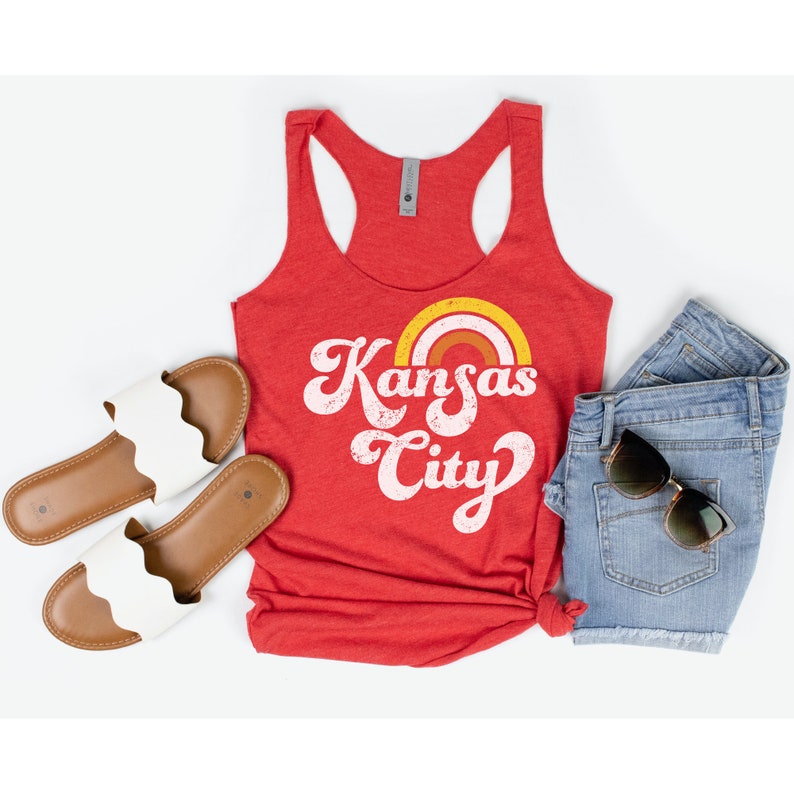 Puede incluir: Camiseta de tirantes roja con un gr&aacute;fico blanco que dice "Kansas City" con un dise&ntilde;o de arco&iacute;ris sobre el texto.