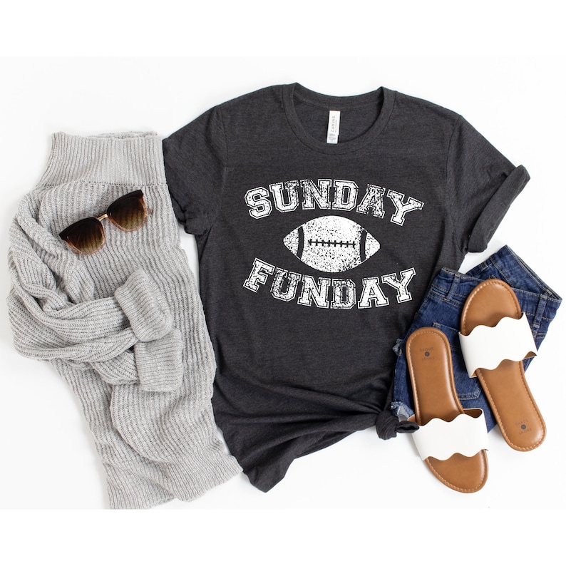 Op de afbeelding: Een donker grijs t-shirt met een witte afbeelding van een voetbal en de tekst "SUNDAY FUNDAY".