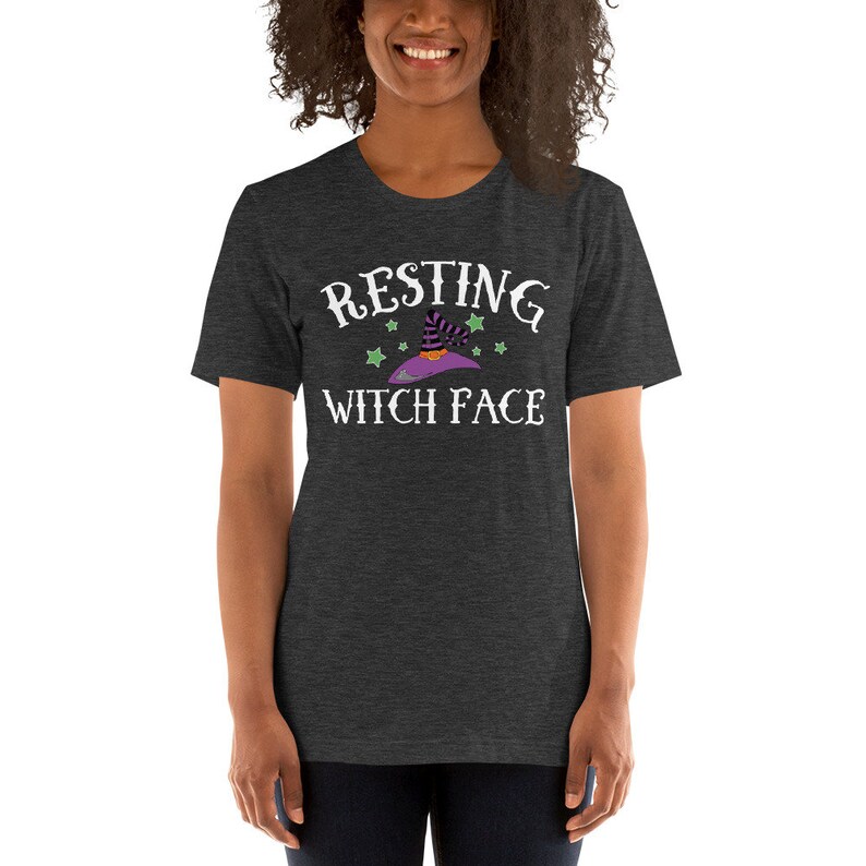 Puede incluir: Una camiseta gris oscuro jaspeada con un gr&aacute;fico blanco que dice "Resting Witch Face" con un sombrero de bruja de dibujos animados y estrellas.