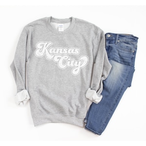 May include: A gray sweatshirt with a white retro-style graphic that says "Kansas City".