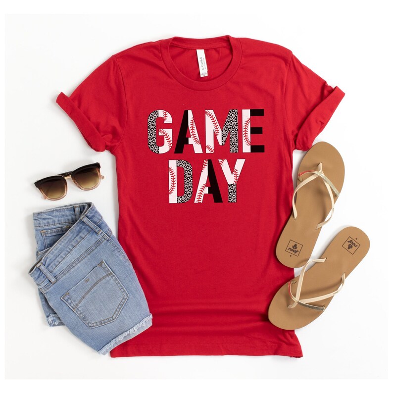 May include: Red t-shirt with the words "GAME DAY" in black letters with a baseball and leopard print design.