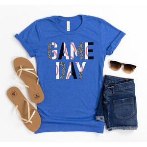 May include: A royal blue t-shirt with the words "GAME DAY" printed in black letters. The letters are made up of a baseball pattern with white and red stitching.