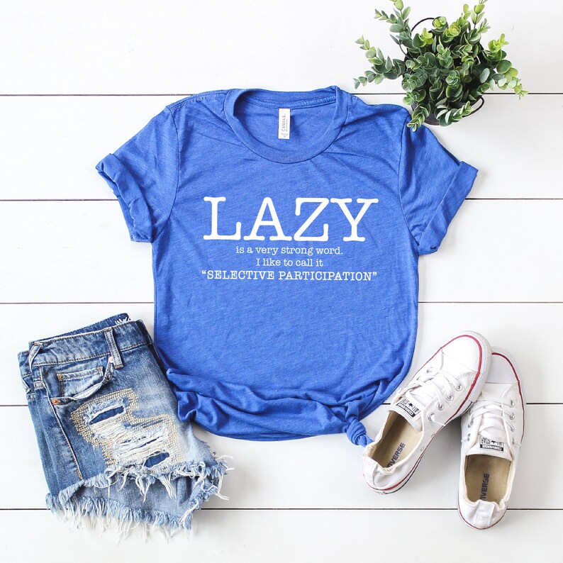 Op de afbeelding: Een blauw T-shirt met de tekst "LAZY is a very strong word. I like to call it "SELECTIVE PARTICIPATION""