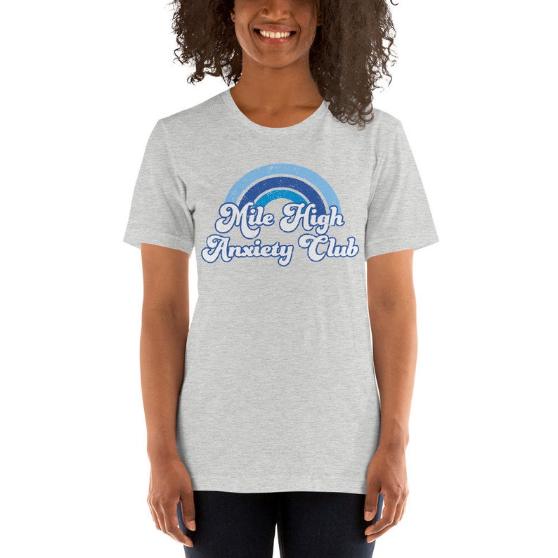 May include: A gray t-shirt with a blue and white rainbow graphic and the text "Mile High Anxiety Club" in a retro font.