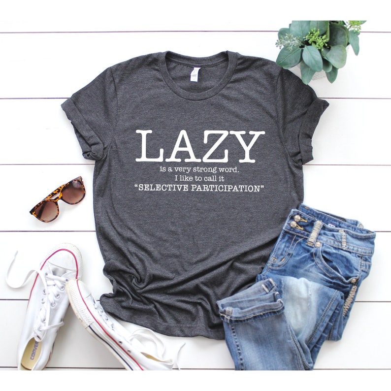 Op de afbeelding: Grijs T-shirt met witte tekst die luidt: "LAZY is a very strong word. I like to call it "SELECTIVE PARTICIPATION""