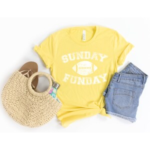 Op de afbeelding: Geel T-shirt met een witte afbeelding waarop "SUNDAY FUNDAY" staat met een voetbal in het midden van de tekst.