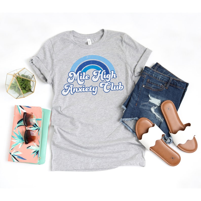 May include: Gray t-shirt with a blue and white rainbow graphic and the text "Mile High Anxiety Club" in a retro font.