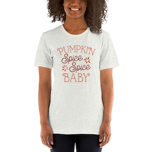 Op de afbeelding: Lichtgrijs t-shirt met de tekst "PUMPKIN Spice Spice Spice BABY" in oranje en bordeauxrood. De tekst is versierd met bloemmotieven. Het t-shirt heeft een ronde hals en korte mouwen.
