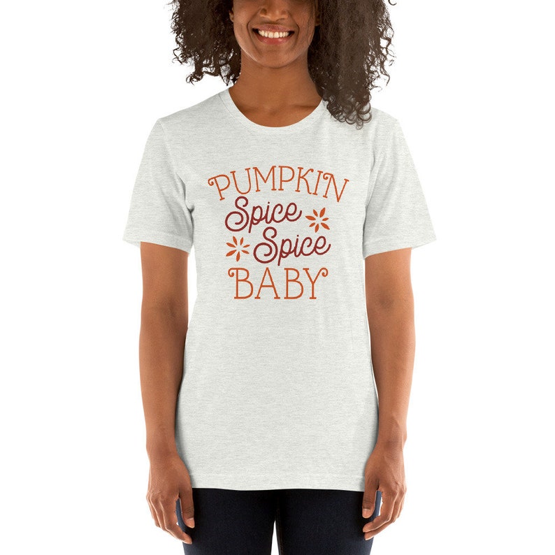 Op de afbeelding: Lichtgrijs t-shirt met de tekst "PUMPKIN Spice Spice Spice BABY" in oranje en bordeauxrood. De tekst is versierd met bloemmotieven. Het t-shirt heeft een ronde hals en korte mouwen.