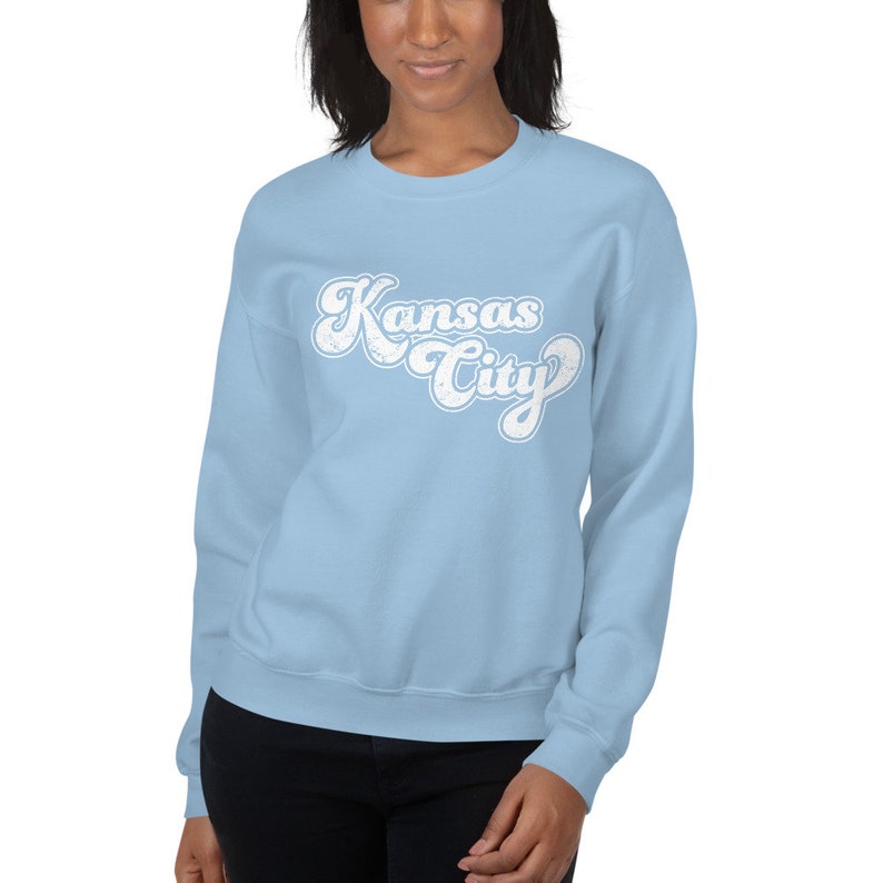 May include: A light blue sweatshirt with a white retro-style graphic that says "Kansas City".