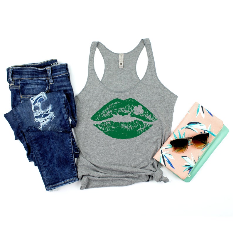 Puede incluir: Un top de tirantes gris con un estampado de beso verde y un tr&eacute;bol. El top se combina con unos vaqueros azules y un bolso de mano floral.