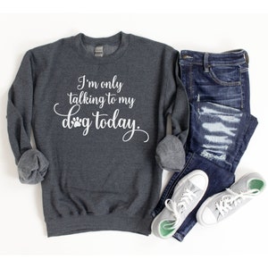May include: A dark grey sweatshirt with the text "I'm only talking to my dog today." in white lettering. The sweatshirt is shown on a white background with a pair of blue jeans and white trainers.