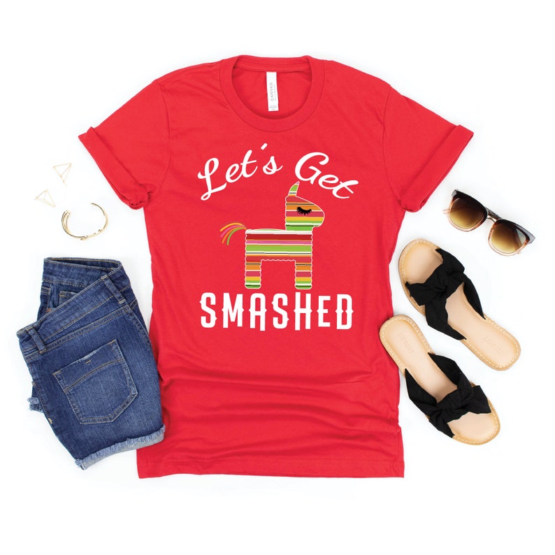 May include: Red t-shirt with white text that says "Let's Get Smashed" and a cartoon image of a pinata.