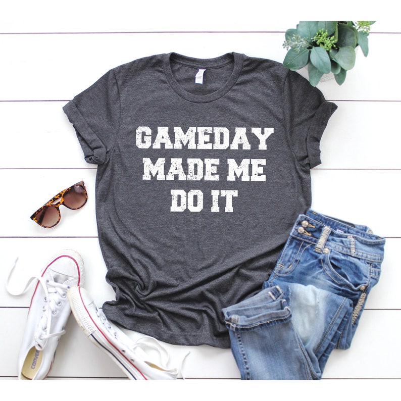 May include: A dark gray t-shirt with the text "GAMEDAY MADE ME DO IT" in white distressed lettering.