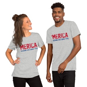May include: Two people wearing grey t-shirts with the text "'MERICA KICKING ASS SINCE 1776" in red and blue lettering.
