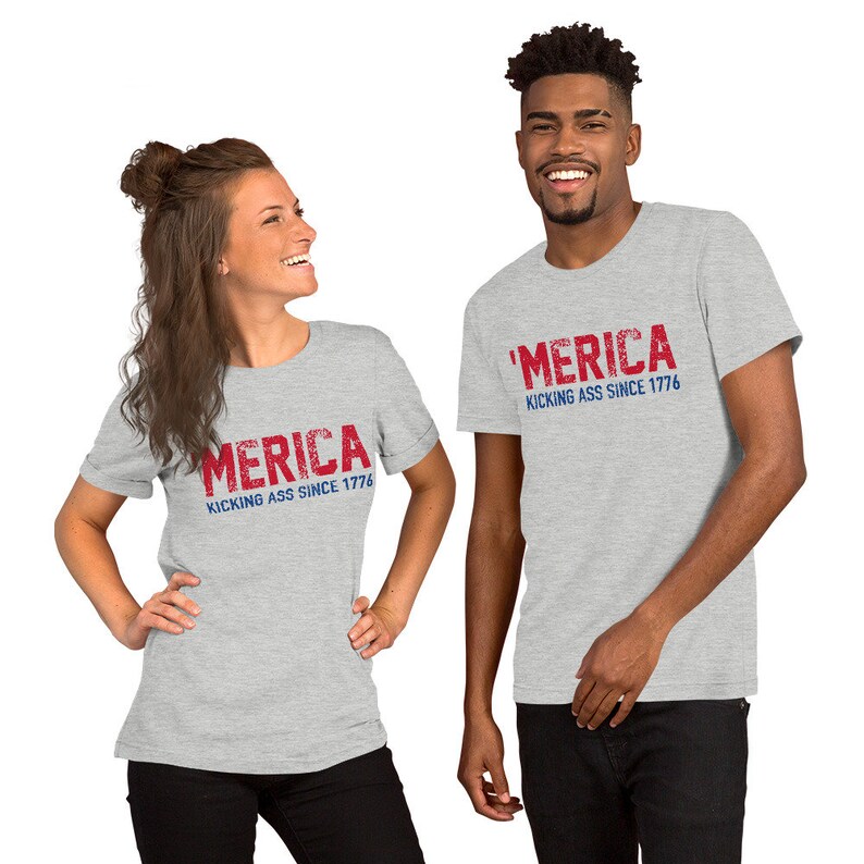 May include: Two people wearing grey t-shirts with the text "'MERICA KICKING ASS SINCE 1776" in red and blue lettering.