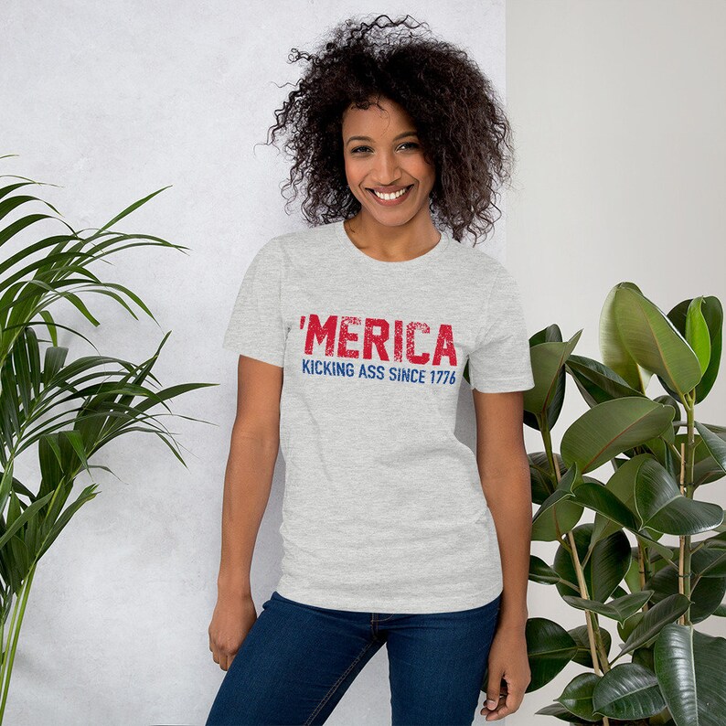 May include: A heather grey t-shirt with a red and blue distressed graphic that says "'MERICA KICKING ASS SINCE 1776"