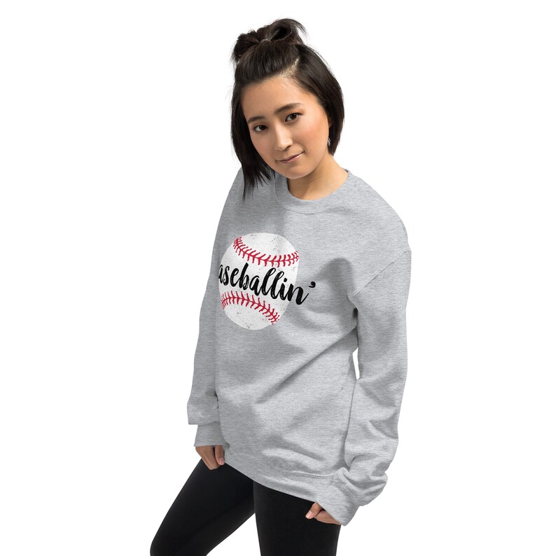 May include: A light gray sweatshirt featuring a distressed baseball graphic with red stitching and the word "baseballin'" in a script font. The sweatshirt is made of a soft material and is suitable for casual wear.