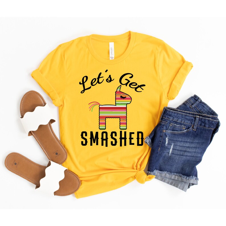May include: Yellow t-shirt with a black graphic of a pinata and the text "Let's Get Smashed".