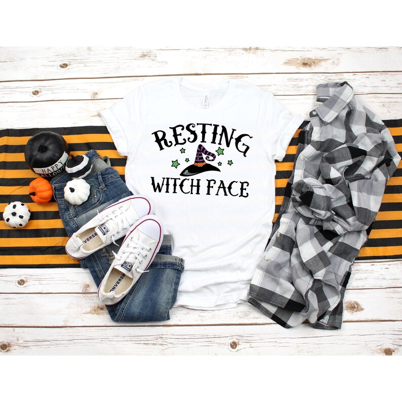 Puede incluir: Camiseta blanca con texto negro que dice "Resting Witch Face" y un sombrero de bruja negro y morado con estrellas verdes encima.