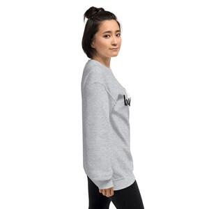 May include: A light gray sweatshirt with the word "baby" printed in black script. The word "baby" has a red heart above the "b". The sweatshirt is made of a soft material.