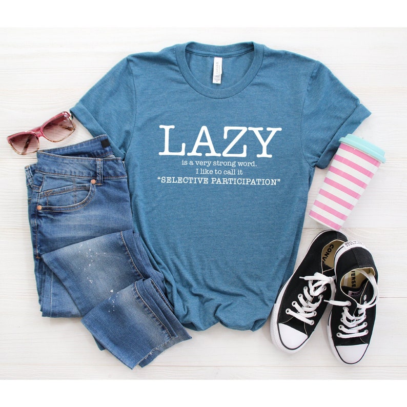Op de afbeelding: Een tealblauw t-shirt met witte tekst die "LAZY is a very strong word. I like to call it "SELECTIVE PARTICIPATION" zegt.