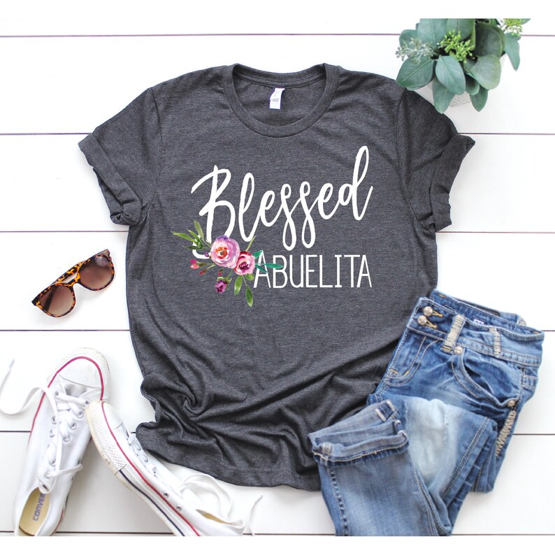 May include: A dark grey t-shirt with the text "Blessed Abuelita" in white lettering and a floral design.