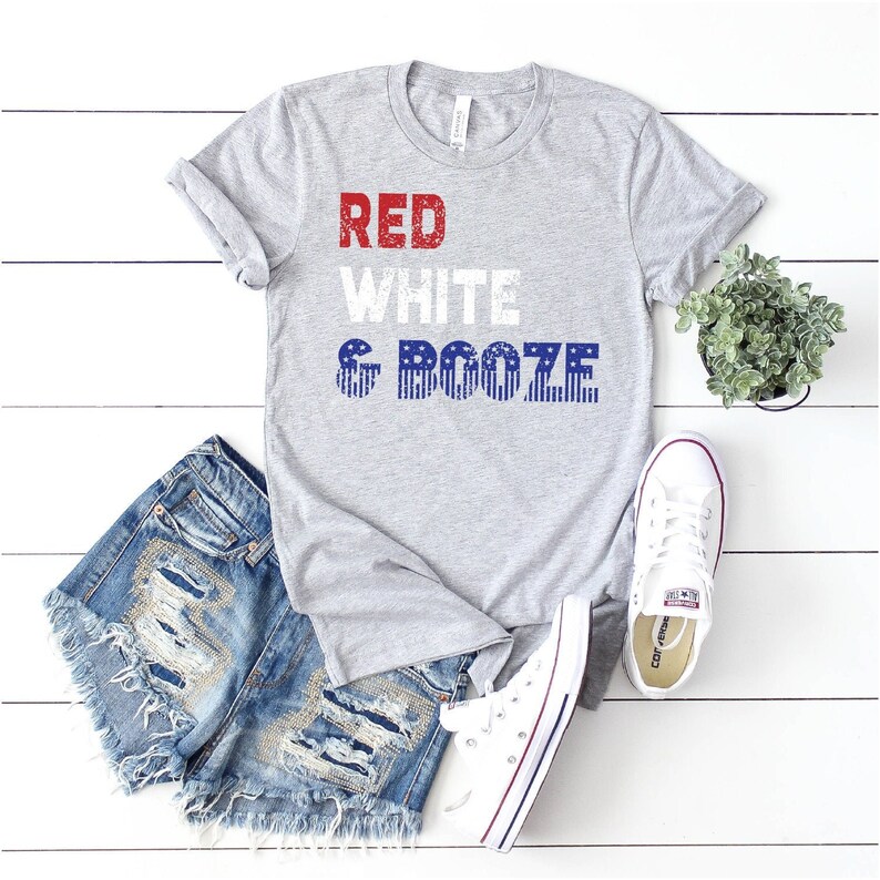May include: A gray t-shirt with the text "RED WHITE & BOOZE" in red, white, and blue with a distressed look. The text is in a stacked format with the word "BOOZE" featuring a red, white, and blue American flag pattern.