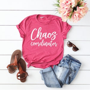 以下が含まれることがあります： 白い文字で「Chaos coordinator」と書かれたピンクのTシャツ