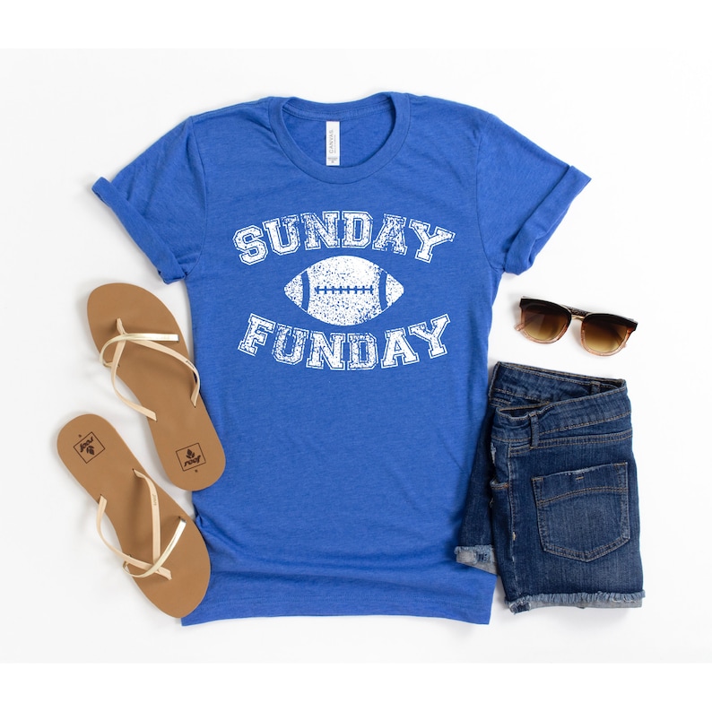 Op de afbeelding: Een koninklijk blauw t-shirt met een witte, verweerde afbeelding met de tekst "SUNDAY FUNDAY" met een voetbal in het midden.
