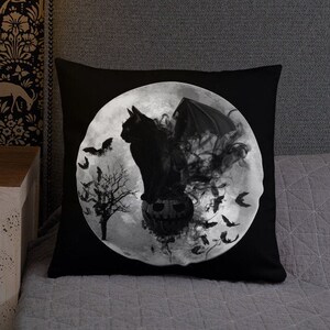 May include: Black and white Halloween pillow featuring a black cat with wings sitting on a jack-o-lantern in front of a full moon.