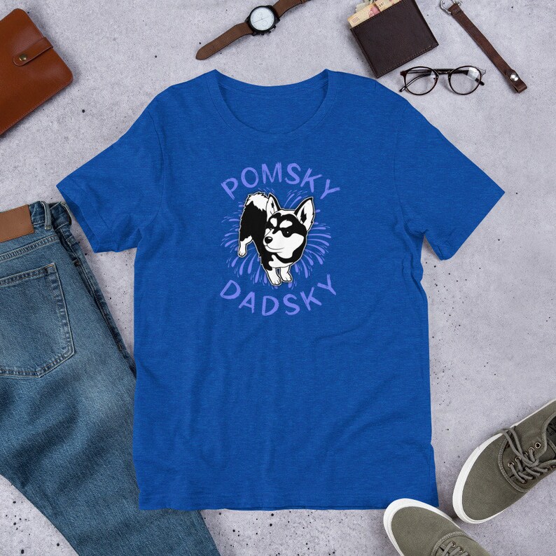 May include: A royal blue t-shirt with a white and black cartoon dog illustration. The text "Pomsky Dadsky" is printed in purple on the shirt.
