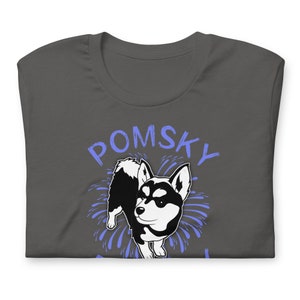 May include: A dark gray t-shirt with a blue and white illustration of a Pomsky dog with fireworks behind it. The text "POMSKY" is written in blue above the dog.