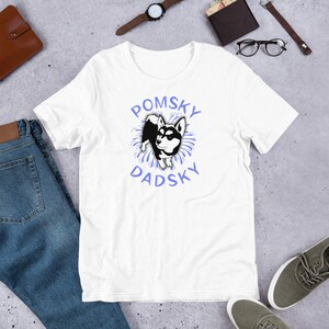 May include: White t-shirt with a blue and white graphic of a black and white dog with the text "Pomsky Dadsky" in blue.