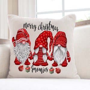 Puede incluir: Almohada blanca con un dise&ntilde;o de gnomo navide&ntilde;o rojo y blanco. La almohada presenta tres gnomos con sombreros rojos y barbas blancas. El texto "merry christmas gnomies" est&aacute; impreso en la almohada.
