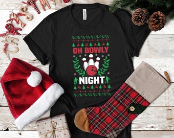 May include: Black t-shirt with a Christmas-themed bowling design. The shirt features a green and white pattern with a red bowling ball and pins. The text "Oh Bowly Night" is printed in white on the shirt.
