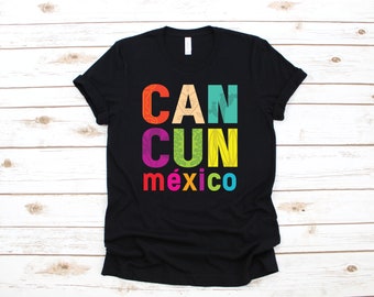 Op de afbeelding: Zwart T-shirt met het woord "CANCUN" in grote, kleurrijke letters. Het woord "méxico" staat eronder in kleinere, veelkleurige letters. De letters hebben verschillende patronen en texturen.