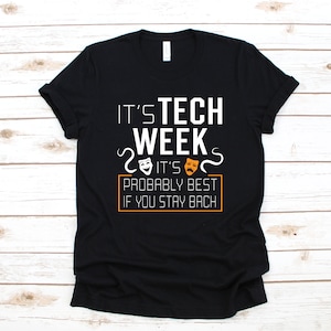 Puede incluir: Camiseta negra con texto blanco que dice "It's Tech Week It's Probably Best If You Stay Back" con dos máscaras blancas y naranjas a cada lado del texto.
