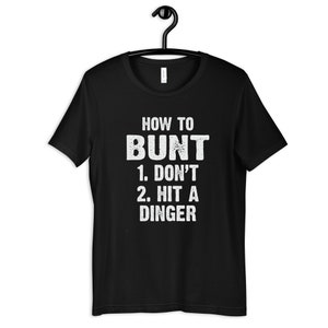 May include: Black t-shirt with white text that reads "How to Bunt 1. Don't 2. Hit a Dinger"