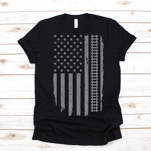 May include: A black t-shirt with a distressed grey American flag design featuring railway tracks.
