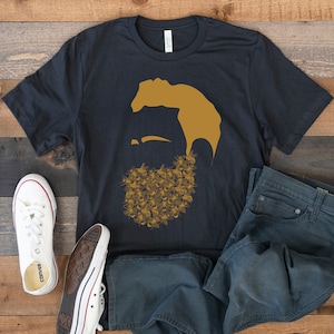 May include: A black t-shirt with a graphic of a man's face with a beard made of bees. The graphic is in shades of yellow and brown.