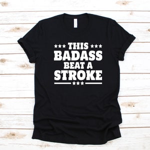 May include: Black t-shirt with white text that reads "This badass beat a stroke" with stars above and below the text.