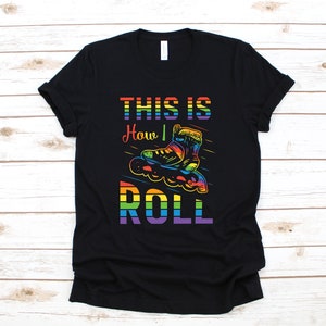 Op de afbeelding: Zwart T-shirt met een regenboogontwerp en de tekst "This is How I Roll" met een regenboog-rolschaatsgrafiek.