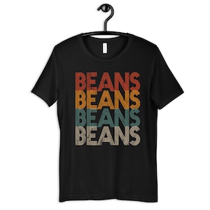 May include: Black t-shirt with a retro-style graphic that says "BEANS" four times in stacked rows. Each "BEANS" is a different color, with the top one being red, the second orange, the third teal, and the bottom one beige.