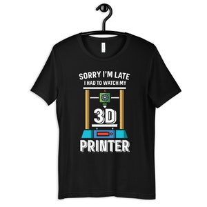 Op de afbeelding: Zwart T-shirt met een witte afbeelding van een 3D-printer en de tekst "Sorry, ik ben te laat, ik moest mijn 3D-printer bekijken".