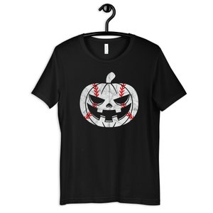 Puede incluir: Camiseta negra con un gráfico de calabaza de béisbol blanco y rojo. La calabaza tiene una cara de miedo y el béisbol tiene costuras rojas.